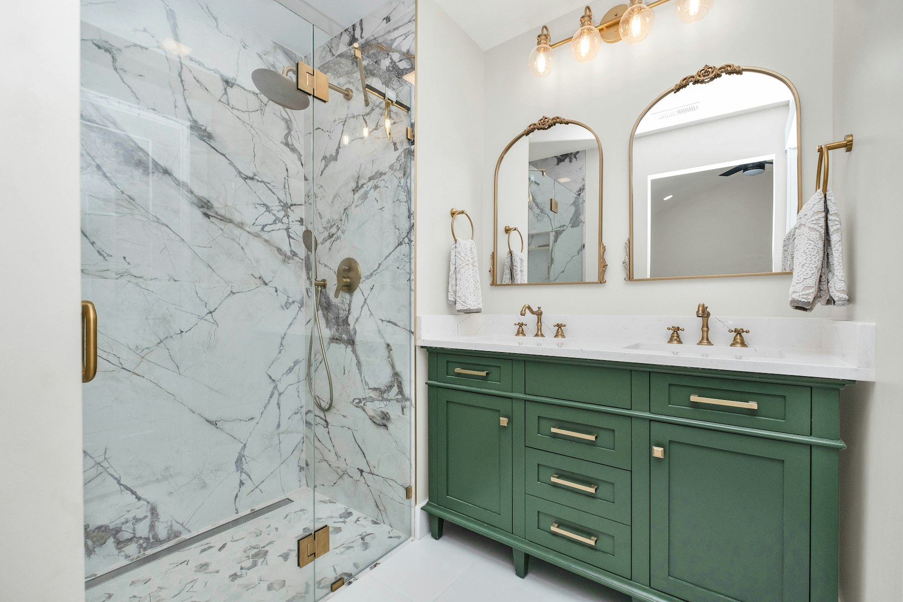Bathroom remodel with a marble shower surround, green vanity and brass fixtures